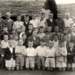 
						Possibly class photo of boys (aged c. 8-12) with teacher or carer posed in front of huts in Tengeru Displaced Persons Camp, Tangyanika, 1943-1950. Edmund Moskal is possibly in the photo					