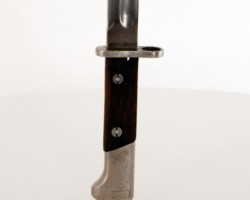 Polish bayonet wz. 1928
Manufactured by Fabryka Broni in Radom. Bayonets of this type were used by the Border Guard and the Border Protection Corps.
Construction:
A single-edged blade with a two-sided concave groin. Convex two-sided cut, single-edged symmetrical tongue. Handle with wooden covers attached to the shaft with two bolts and nuts. Handle with a fire shield overlapping the back of the head. Mounting on the rifle in the handle guide with the barrel supporting the concave milling of the handguard. Hole for the rod with drainage through the cuts at the bottom of the covers. Clasp with a spiral spring. Steel sheath with a knob at the bottom, with a clip soldered together with a strengthening oval washer to the sheath of the scabbard. Elongated catch at the top to make it easier to remove the frog. A gland with two flat springs and a spur, attached to the sheath with a single screw. It differs in characteristics from wz.1924 in the following details: - a 1 mm wider pommel in the sill, a wider groove - 14 mm, a thicker scabbard about 1 mm at the top, mounting the gland with two rivets on both sides of the scabbard. Dimensions:
Bayonet length - 384 mm, bayonet length in the scabbard - 402 mm, blade length - 253 mm, blade width in the fret - 26 mm, handle length - 125.5 mm, crossguard thickness - 5.5 mm, inner ring diameter - 15, 5 mm, the length of the scabbard - 271 mm. Zbigniew Kulon's collection